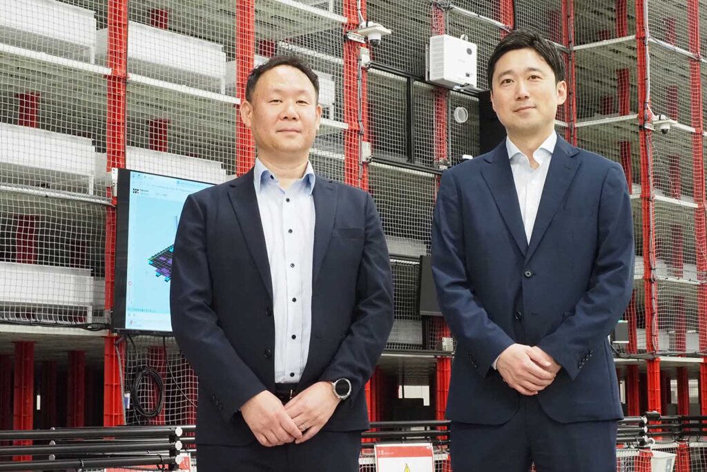 株式会社アルプス物流 保管BU 部長 野殿征範氏（左）と
同社経営企画部 経営企画課 課長 渡邊真広氏（右）。大栄倉庫導入のラピュタASRS前で。